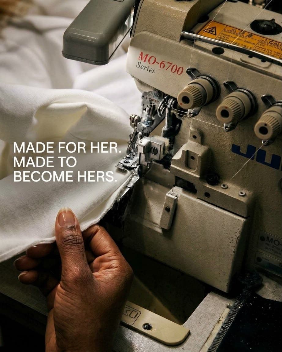 A seamstress's hand guiding white fabric through an industrial overlock sewing machine